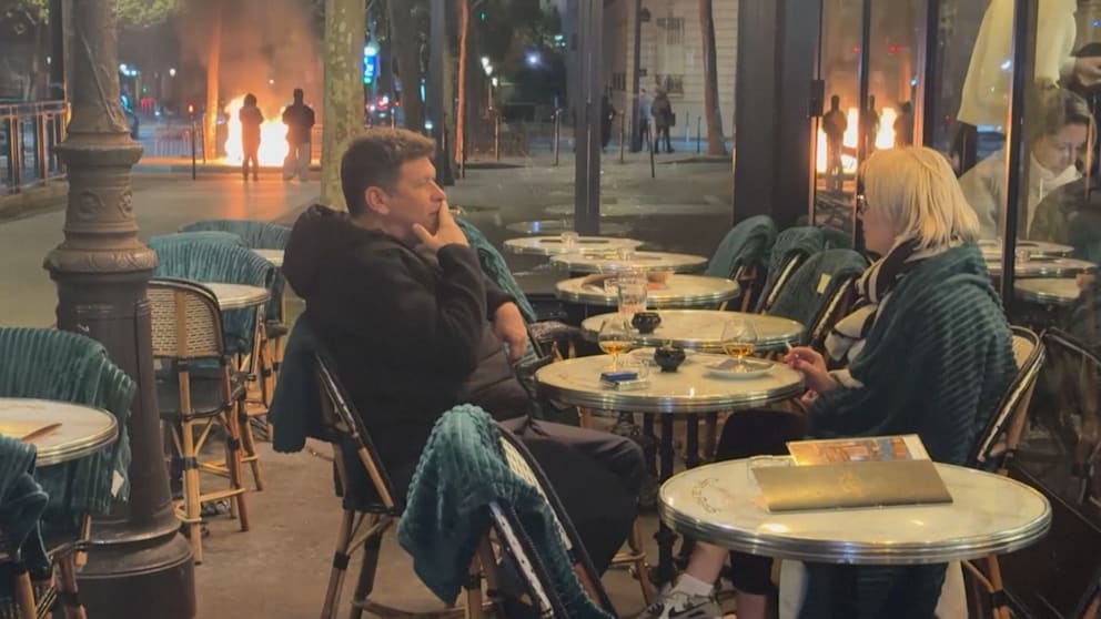 Krawalle am Triumphbogen: Pärchen schlürft Drinks vor brennenden Barrikaden